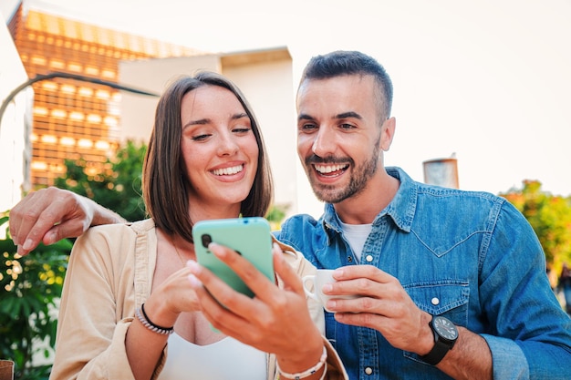 Foto casal caucasiano real usando um dispositivo de telefone celular para pesquisar na internet dois amigos compartilhando no