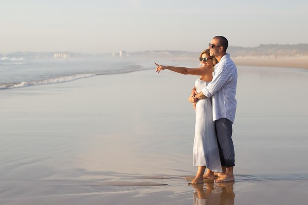 Casal caucasiano satisfeito passando tempo na praia. Marido e mulher em roupas casuais andando na areia molhada. Viajar, relaxamento, felicidade, conceito de família