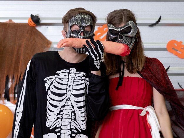 Foto casal caucasiano vestindo traje de halloween com máscara de fantasma assustadora comendo braço falso com sangue