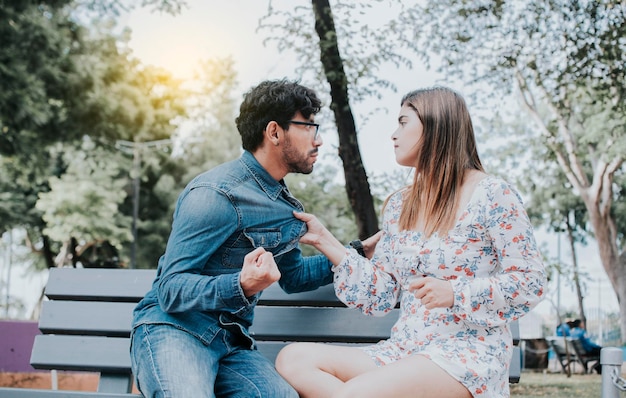 Casal chateado discutindo em um banco de parque Jovem casal discutindo sentado em um banco de parque Conceito de casais agressivos no parque Homem discutindo com sua namorada sentada em um parque