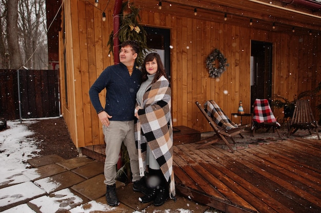 Casal coberto cobertor no dia de inverno, passando tempo juntos no amor contra a casa de madeira
