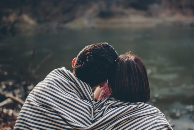 Casal coberto com cobertor fazendo carinho no lago