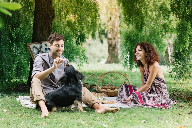 Casal com cachorro fazendo piquenique em um parque