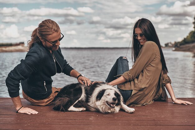 Casal com cachorro. Lindo casal jovem brincando com um cachorro sentado perto do lago ao ar livre