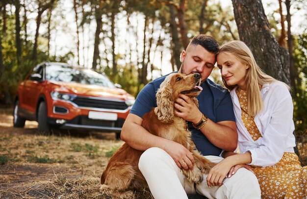 Casal com cachorro tem fim de semana ao ar livre na floresta com o carro atrás deles.