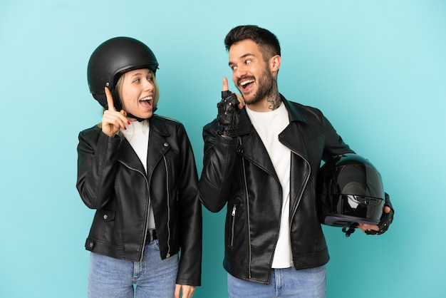 Casal com capacete de motociclista sobre fundo azul isolado com a intenção de perceber a solução enquanto levanta um dedo