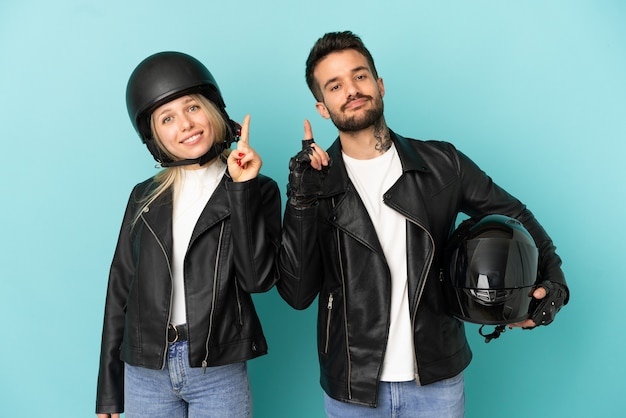 Foto casal com capacete de motociclista sobre fundo azul isolado mostrando e levantando um dedo em sinal dos melhores