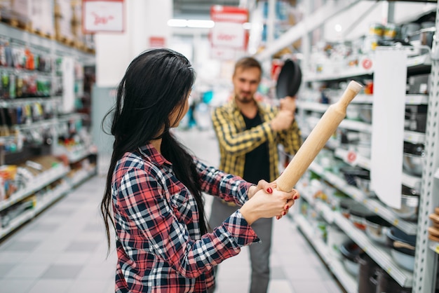 Casal com frigideira e rolo no supermercado