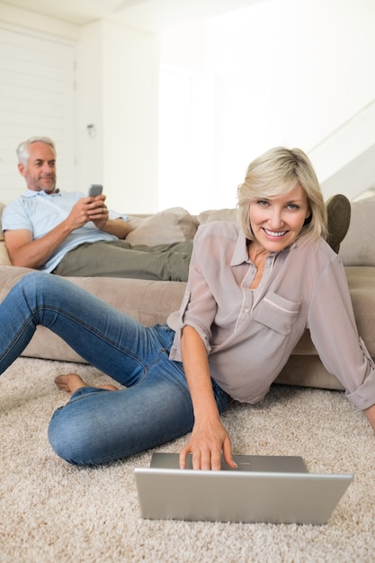 Casal com laptop e celular na sala de estar em casa