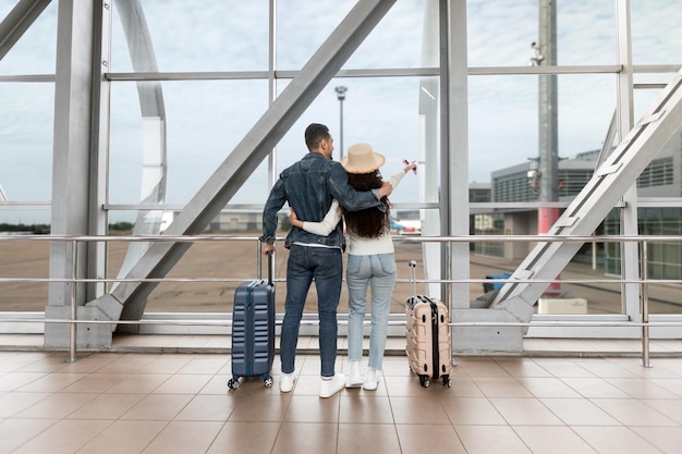 Casal com malas olhando da janela no aeroporto enquanto espera o voo