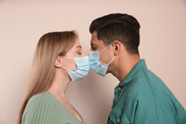 Casal com máscaras médicas tentando se beijar em fundo bege