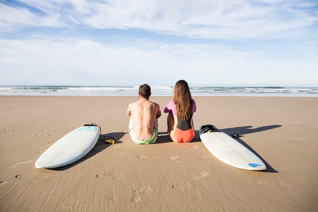 Casal com pranchas de surf sentado na praia