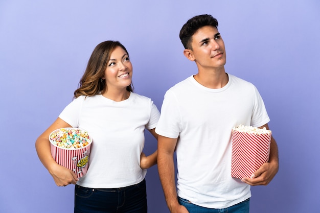 Casal comendo pipoca enquanto assiste a um filme roxo olhando para cima enquanto sorri