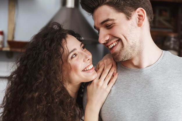 Casal contente, homem e mulher, sorrindo e se abraçando na cozinha moderna de casa