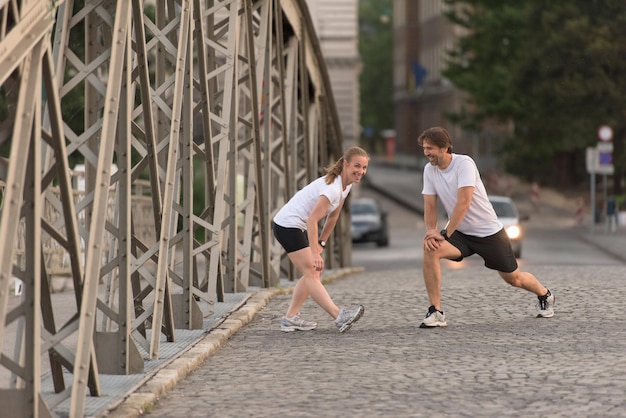 casal correndo aquecendo e alongando antes do treino de corrida matinal na cidade com o nascer do sol ao fundo