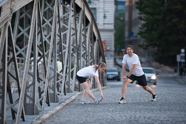 casal correndo aquecendo e alongando antes do treino de corrida matinal na cidade com o nascer do sol ao fundo