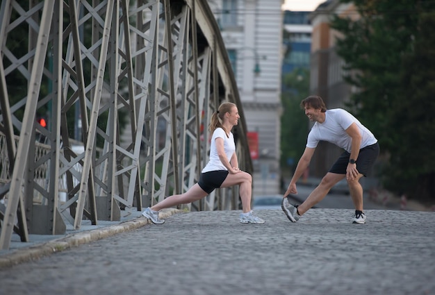 casal correndo aquecendo e alongando antes do treino de corrida matinal na cidade com o nascer do sol ao fundo