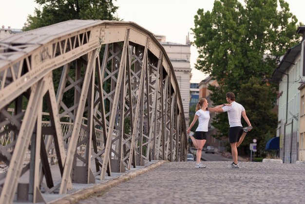 casal correndo aquecendo e alongando antes do treino de corrida matinal na cidade com o nascer do sol ao fundo