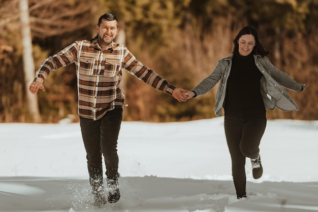 Casal correndo e de mãos dadas na floresta de neve de inverno Foco seletivo