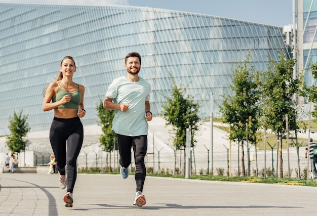 Casal correndo juntos em roupas esportivas perto de arquitetura curva moderna em um dia claro