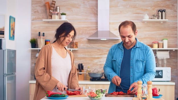 Casal cortando tomates na tábua de madeira para salada saudável na cozinha. cozinhar preparando alimentos orgânicos saudáveis, estilo de vida feliz juntos. refeição alegre em família com legumes