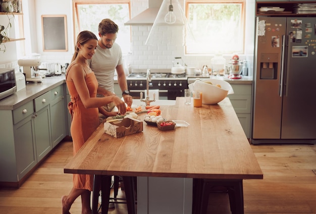 Casal cozinhando comida caseira ou refeição saudável para unir homem e mulher felizes ou divertidos na cozinha de casa juntos Amor de conversa ou jovens no interior moderno com salada de legumes fresca na mesa