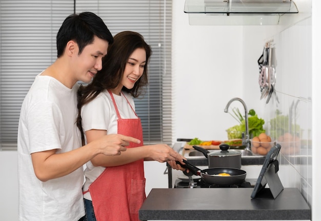 Foto casal cozinhando e preparando comida de acordo com uma receita em um tablet na cozinha em casa