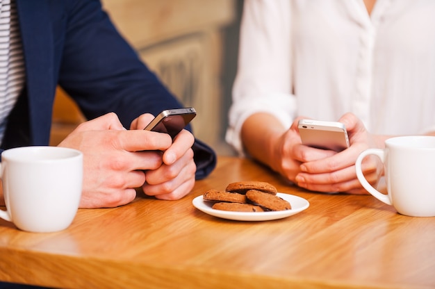 Casal da era digital. close de um casal enviando mensagens de texto em seus celulares enquanto estão sentados em um café