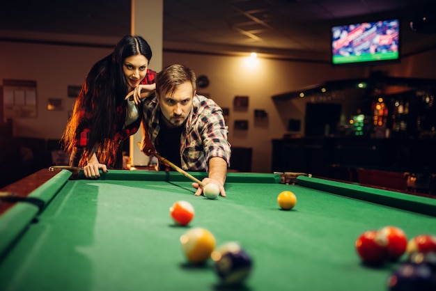 Casal da família joga na sala de bilhar. Lazer masculino e feminino, jogo de sinuca americana no bar desportivo, jogador masculino com objetivo de chute