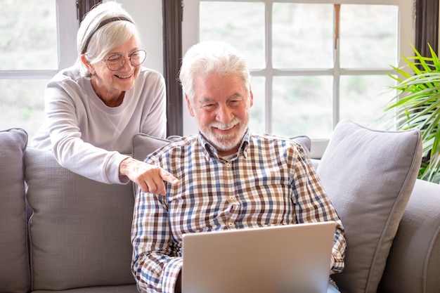 Casal de 70 anos de cabelos brancos feliz em casa usando laptop juntos para fazer compras on-line