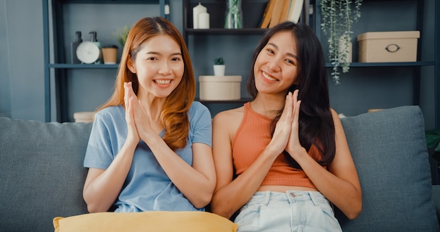 Foto casal de adolescentes asiáticas se sentindo felizes sorrindo e olhando para a frente enquanto relaxam na sala de estar de casa