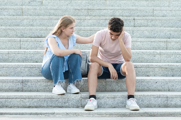 Casal de adolescentes sentado na escada Namorada tentando animar o triste namorado hispânico