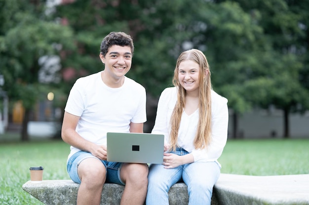 Casal de adolescentes sorrindo para a câmera e usando laptop