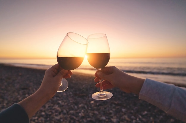 Casal de amantes, bebendo vinho tinto durante assistir o pôr do sol e curtir férias no mar em lua de mel