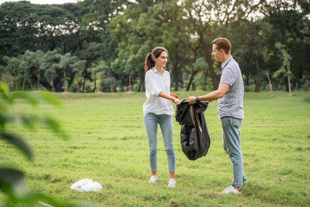 Casal de amantes voluntários usando luvas caminhando para pegar lixo no parque Para manter o ambiente limpo