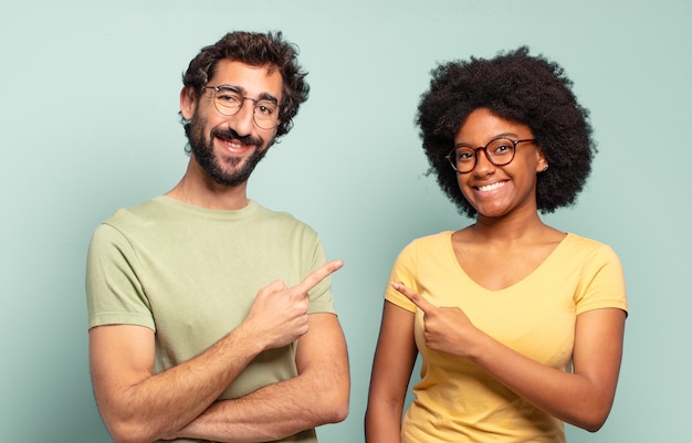 Foto casal de amigos multirraciais sorrindo alegremente, sentindo-se felizes e apontando para o lado e para cima, mostrando o objeto no espaço da cópia