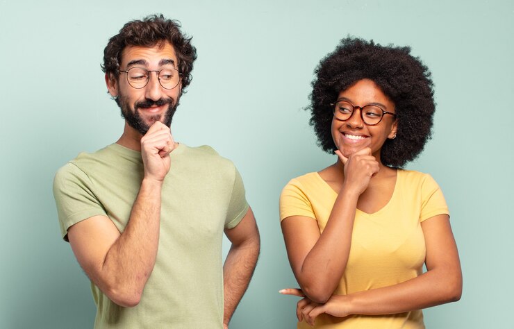 Foto casal de amigos multirraciais sorrindo com uma expressão feliz e confiante com a mão no queixo, pensando e olhando para o lado