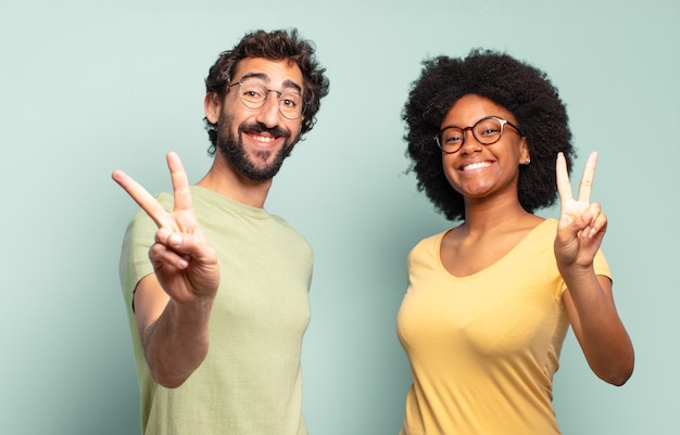 Foto casal de amigos multirraciais sorrindo e parecendo felizes, despreocupados e positivos, gesticulando vitória ou paz com uma das mãos