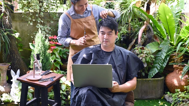 Casal de amor asiático fazendo corte de cabelo para atualizar sua aparência em casa. Trabalho em casa e salão de beleza no jardim.