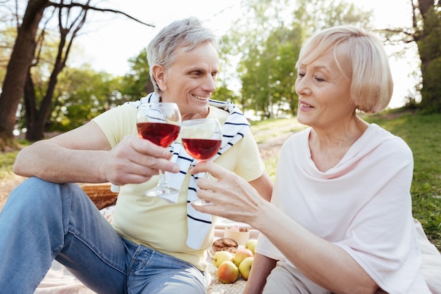 Casal de aposentados feliz e sorridente, expressando positividade enquanto desfruta de um piquenique e bebe vinho