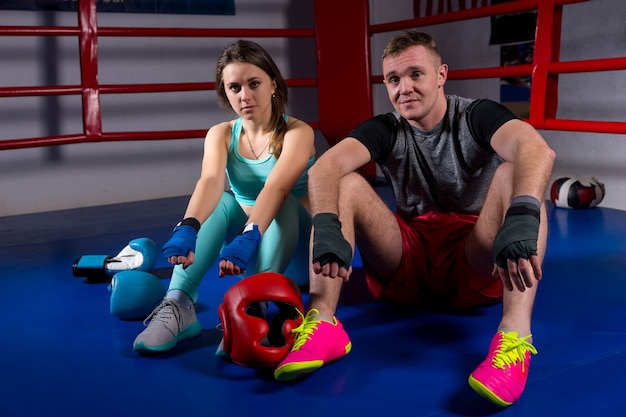 Casal de boxe sentado perto de luvas de boxe e capacete em um ringue de boxe normal em uma academia