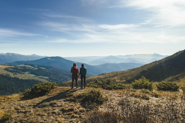 Casal de caminhantes com mochilas na frente da paisagem vale vista no topo de uma montanha