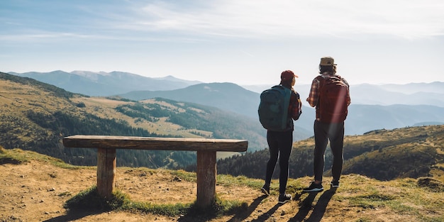 Casal de caminhantes com mochilas na frente da paisagem vale vista no topo de uma montanha