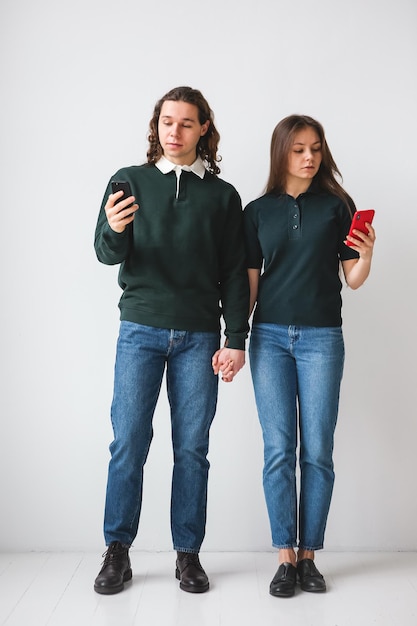 Casal de camisas verdes segurando telefones nas mãos sobre fundo branco jovem e mulher usando telefones