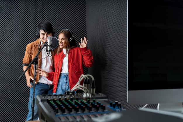 Casal de cantores asiáticos em um estúdio de gravação usando um microfone de estúdio com paixão em um estúdio de gravação de música