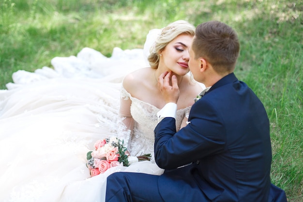 Casal de casamento emocional na grama verde na primavera. amor de duas pessoas. noiva e noivo gentil abraçando e beijando no dia do casamento na natureza. retrato de recém-casados bonitos ao ar livre. conceito de casamento