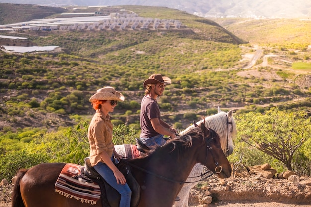 casal de cavaleiro e mulher com cavalos marrons e brancos vão e aproveitam a atividade de lazer ao ar livre em uma excursão viajando pelas montanhas. cowboy moderno e sem tecnologia