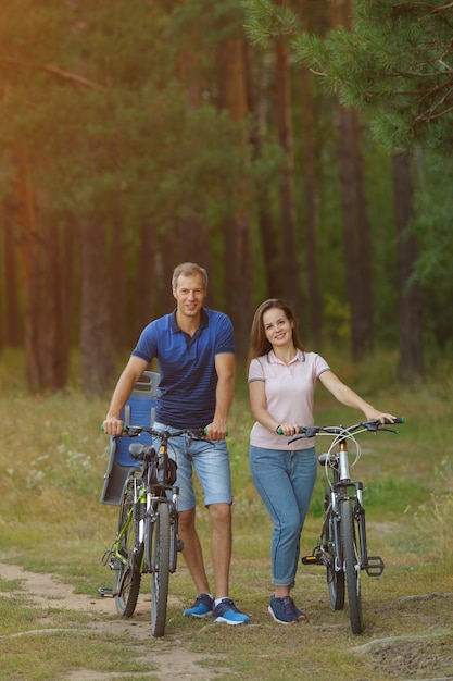 Casal de ciclistas na floresta de pinheiros, passeio romântico. Homem e mulher com bicicletas no parque, pedalando no dia de verão