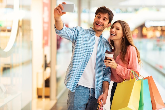 Foto casal de compradores felizes fazendo selfie se divertindo no shopping