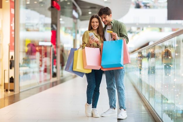 Casal de compras usando telefone e cartão de crédito no shopping